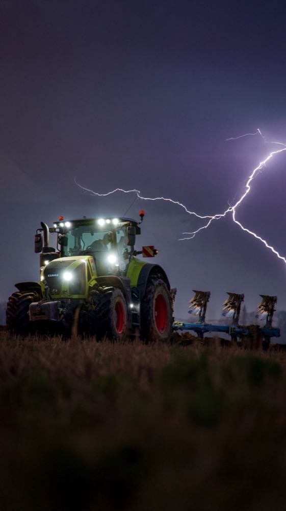 Trattore Agromeccanica Rocchi al lavoro sotto un cielo illuminato dai lampi